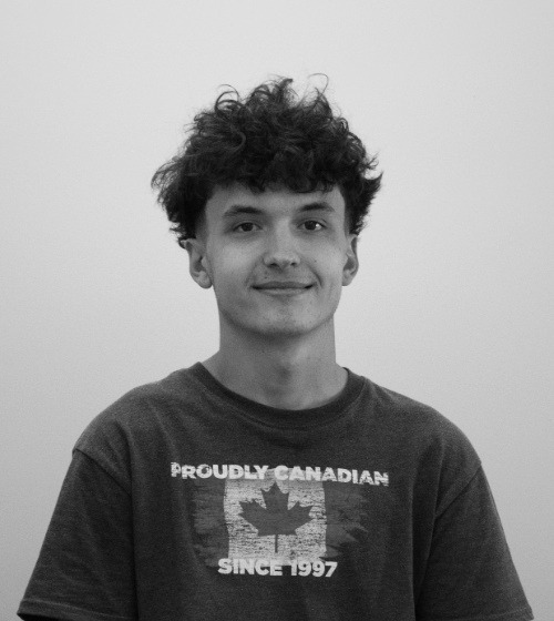 Young person with curly hair wearing a "Proudly Canadian Since 1997" T-shirt, standing against a plain background.